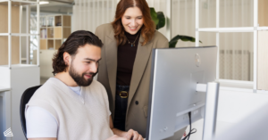 Marcom professionals Lorena en Valentino bekijken samen een computerscherm in een lichte kantooromgeving.