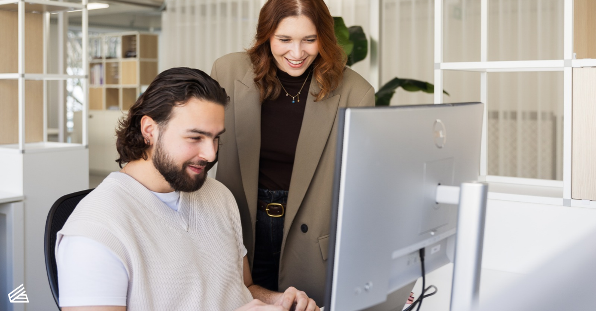 Marcom professionals Lorena en Valentino bekijken samen een computerscherm in een lichte kantooromgeving.