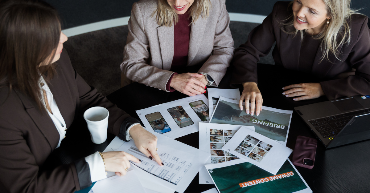 Drie marcom professionals bespreken marketingresultaten en grafieken tijdens een overleg over commerciële strategie en samenwerking.