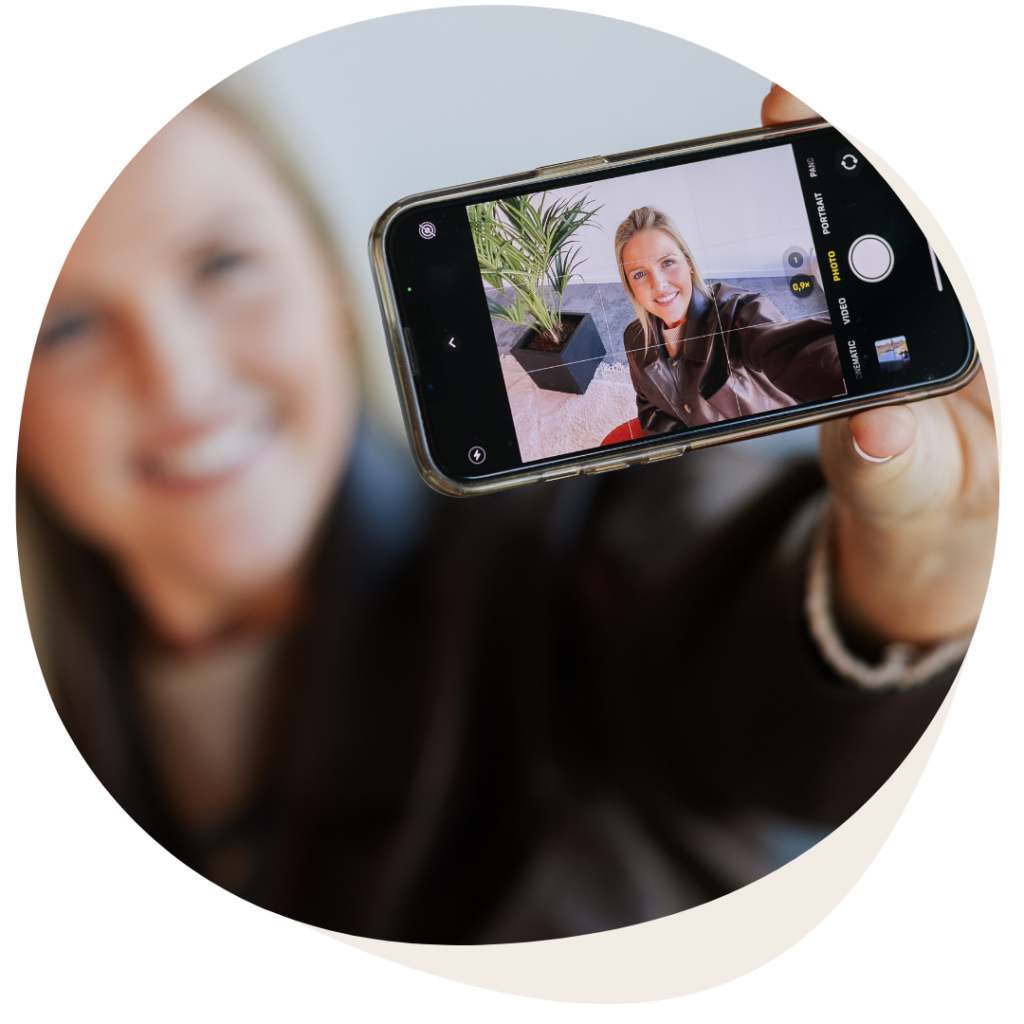 Glimlachende vrouw maakt een selfie met haar smartphone, waarop haar gezicht scherp in beeld verschijnt.