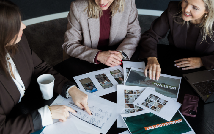 Drie marcom professionals bespreken marketingresultaten en grafieken tijdens een overleg over commerciële strategie en samenwerking.