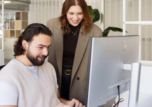 Marcom professionals Lorena en Valentino bekijken samen een computerscherm in een lichte kantooromgeving.