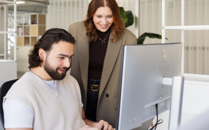 Marcom professionals Lorena en Valentino bekijken samen een computerscherm in een lichte kantooromgeving.